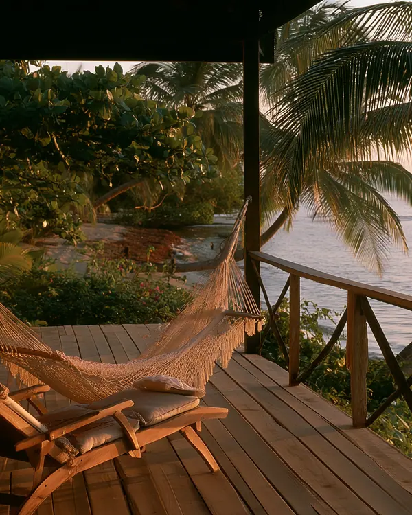 Terrasse en bois avec hamac et chaise longue, vue sur la mer au coucher du soleil