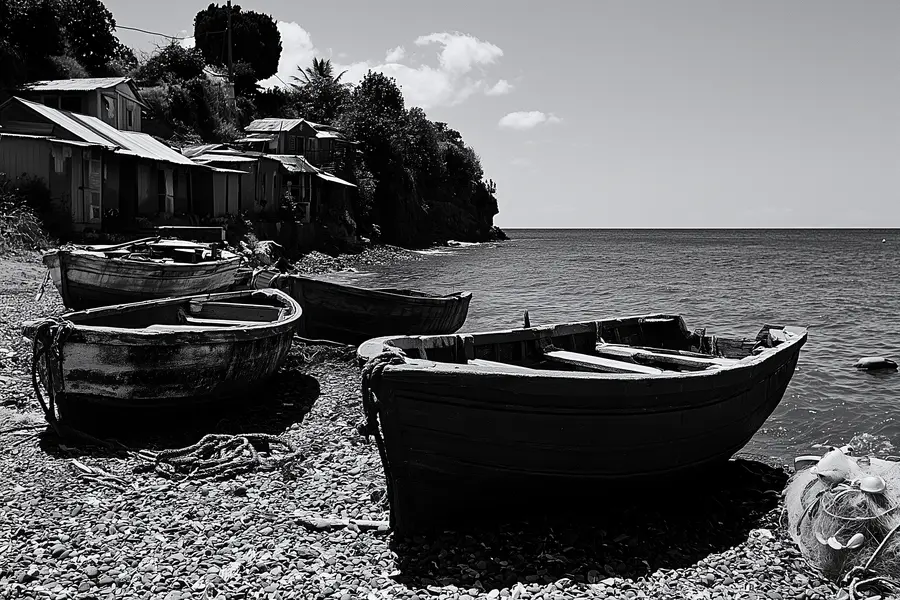 Des yoles de pêche en bois tirées sur une plage de galets, devant des maisons à toit de tôle.