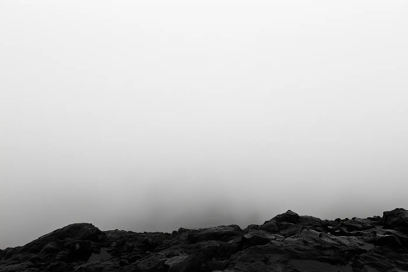 Un mur de nuage blanc occupe presque tout le cadre ; seule une arête de roche noire mouillée reste lisible en bas.